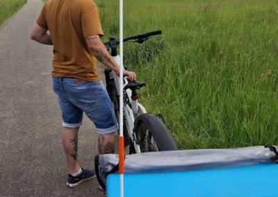 Die jüngste Wege· wartin Mayla fährt im Fahr · rad · anhänger mit. Mayla hat keine Weste. Mayla hat eine Fahne.